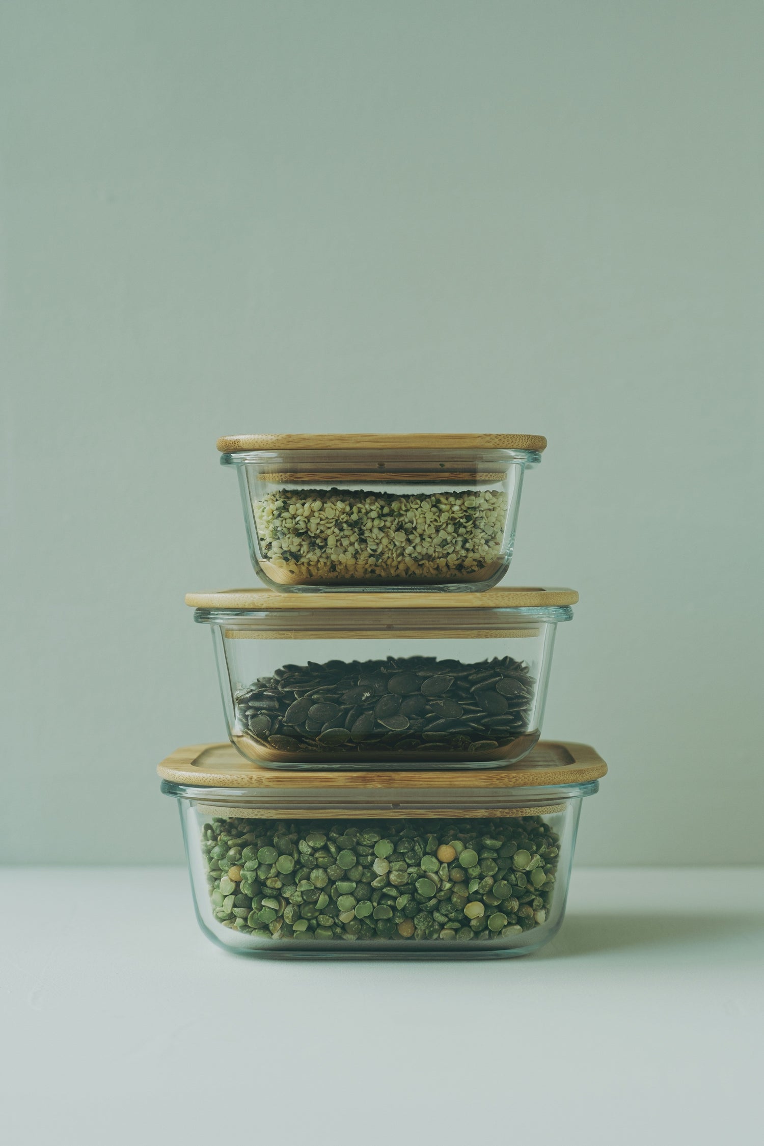 Stacked glass storage containers with bamboo lids, filled with seeds and legumes, ideal for eco-friendly food storage.