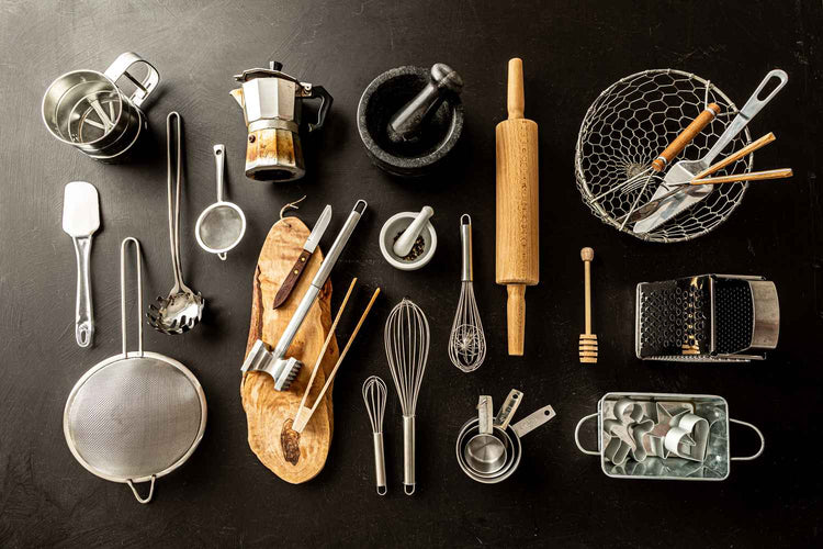 Assorted kitchen tools and gadgets on a black background, including a rolling pin, whisk, mortar and pestle, and grater