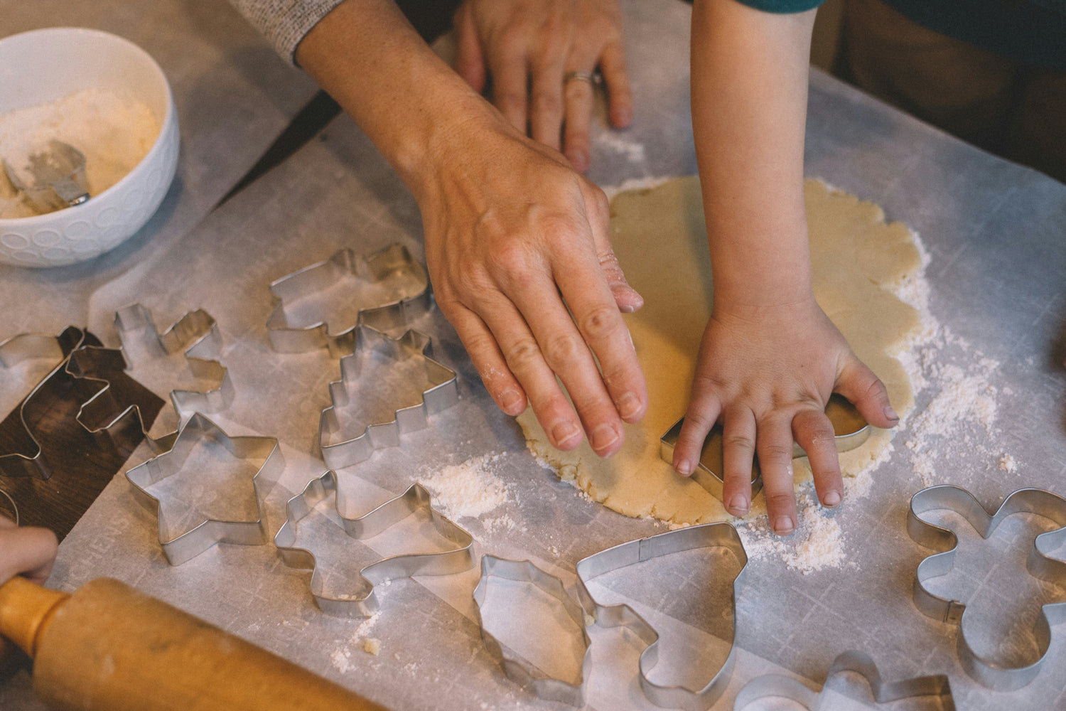 Hands rolling out dough with festive cookie cutters, ideal for baking cookies and holiday treats