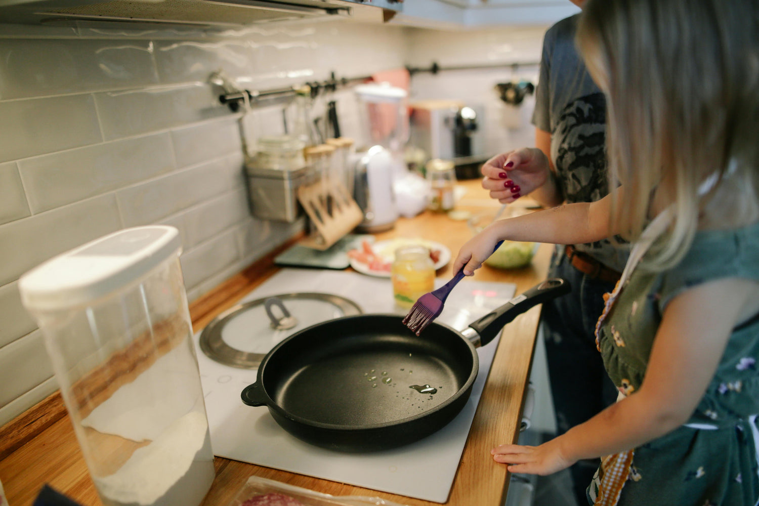 Parent and child cooking together in a modern kitchen, featuring a non-stick frying pan on the stove, promoting family cooking moments